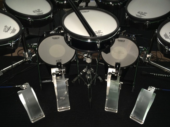 A virtuosodrummer.com image of a symmetrical drumset with longboard kick drum pedals and matching longboard hi-hat pedals inc. remote hi-hat cable drives. The foot pedal hardware is made by TRICK Drums USA.